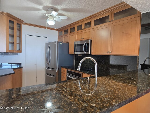 kitchen featuring stainless steel appliances, ornamental molding, a textured ceiling, kitchen peninsula, and dark stone counters