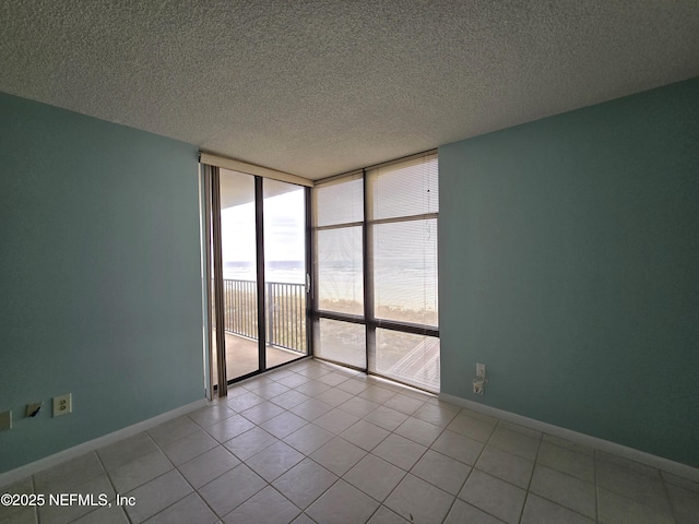 spare room with baseboards, a wall of windows, a textured ceiling, and tile patterned floors