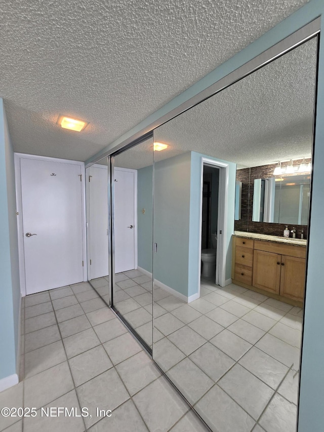 unfurnished bedroom featuring baseboards, a textured ceiling, ensuite bathroom, and light tile patterned floors