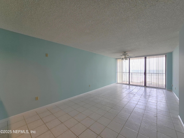 unfurnished room featuring light tile patterned floors, a ceiling fan, expansive windows, a textured ceiling, and baseboards