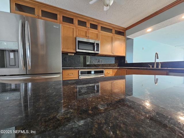 kitchen with brown cabinetry, decorative backsplash, dark stone countertops, stainless steel appliances, and a textured ceiling