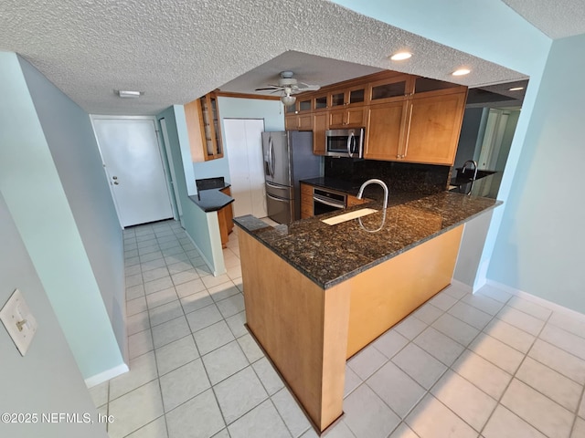 kitchen featuring appliances with stainless steel finishes, glass insert cabinets, a sink, a textured ceiling, and a peninsula