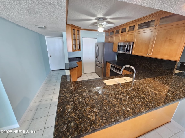 kitchen with light tile patterned floors, dark stone counters, stainless steel appliances, and a sink