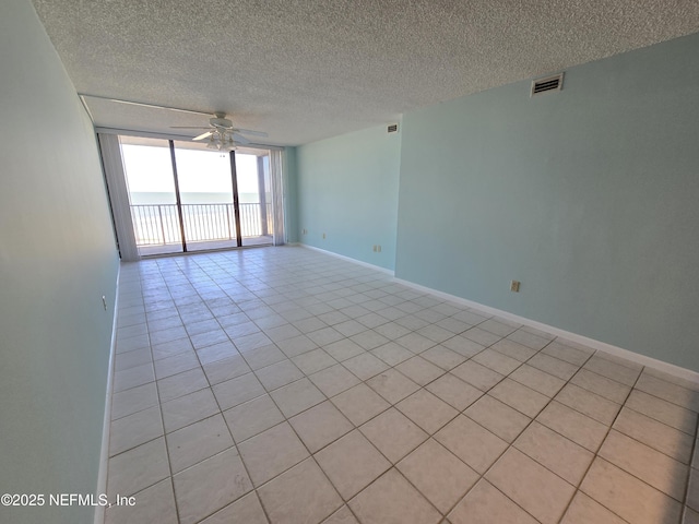 empty room with baseboards, visible vents, a ceiling fan, a wall of windows, and a textured ceiling