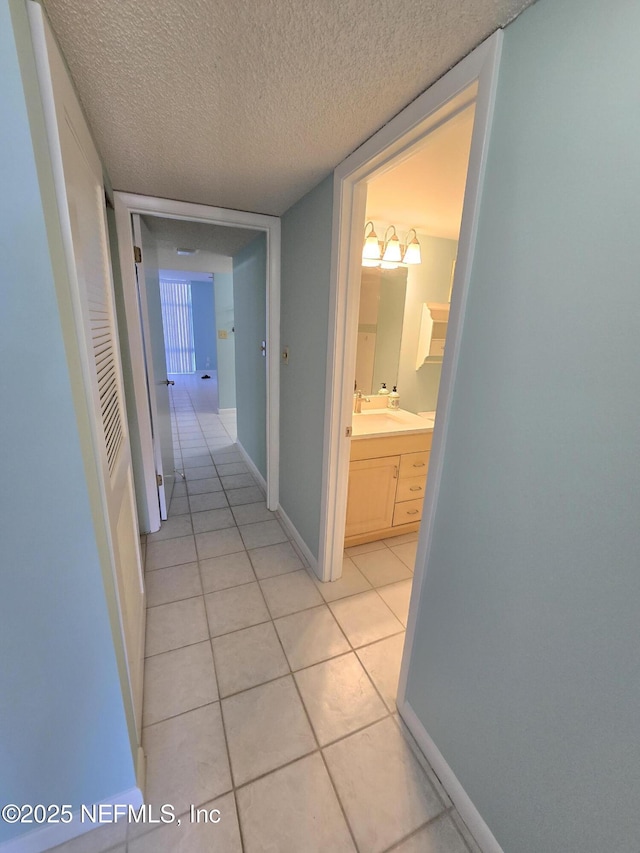 hall with a textured ceiling, light tile patterned floors, a sink, and baseboards