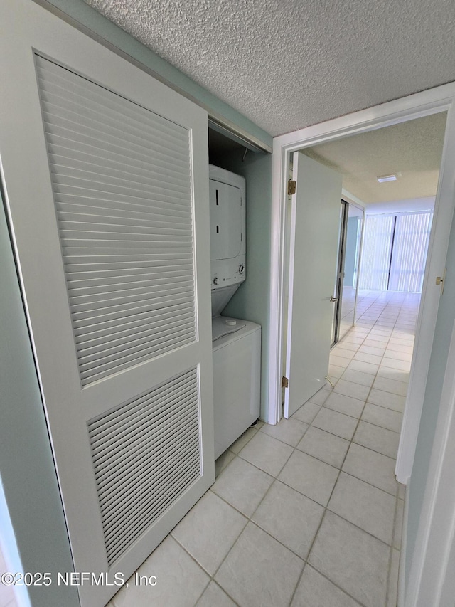 washroom featuring laundry area, a textured ceiling, stacked washing maching and dryer, and light tile patterned floors