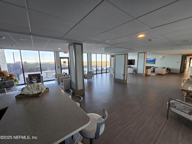 interior space featuring a paneled ceiling, baseboards, and a wall of windows