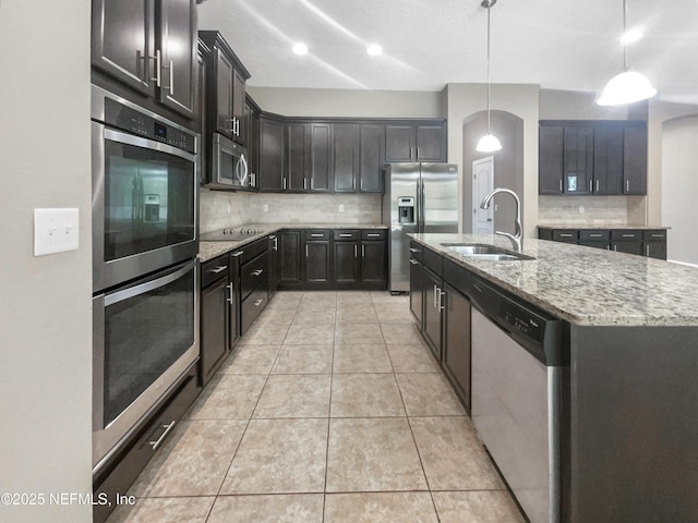 kitchen featuring stainless steel appliances, decorative backsplash, a kitchen island with sink, hanging light fixtures, and sink