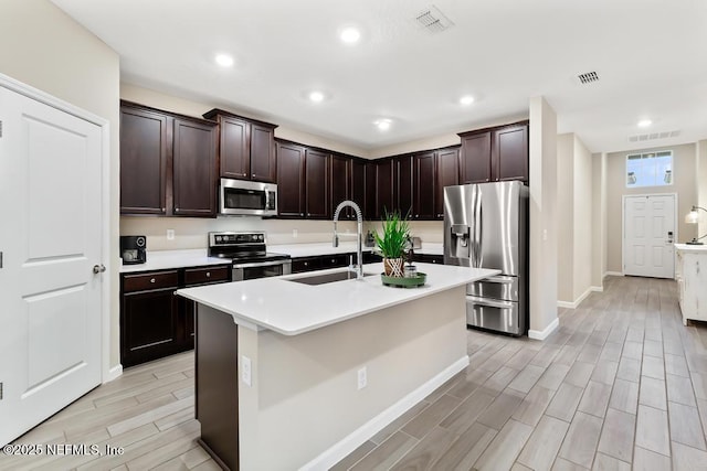 kitchen with sink, a center island with sink, dark brown cabinets, and stainless steel appliances