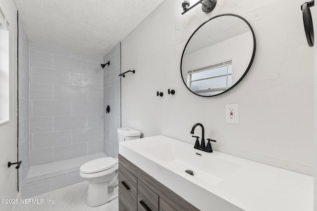 bathroom featuring a tile shower, toilet, a textured ceiling, and vanity