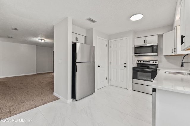 kitchen featuring light carpet, sink, white cabinets, a textured ceiling, and stainless steel appliances