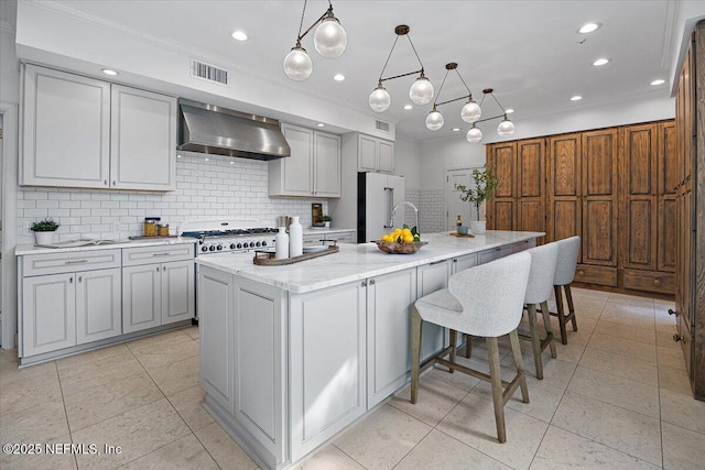 kitchen featuring decorative light fixtures, decorative backsplash, high quality fridge, an island with sink, and wall chimney exhaust hood