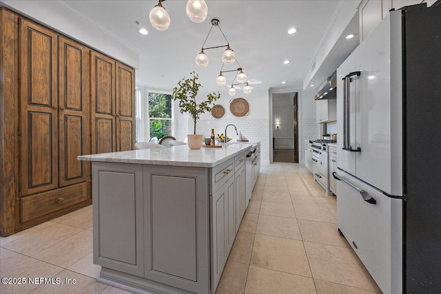 kitchen with a center island with sink, white cabinetry, high end appliances, light stone countertops, and ornamental molding