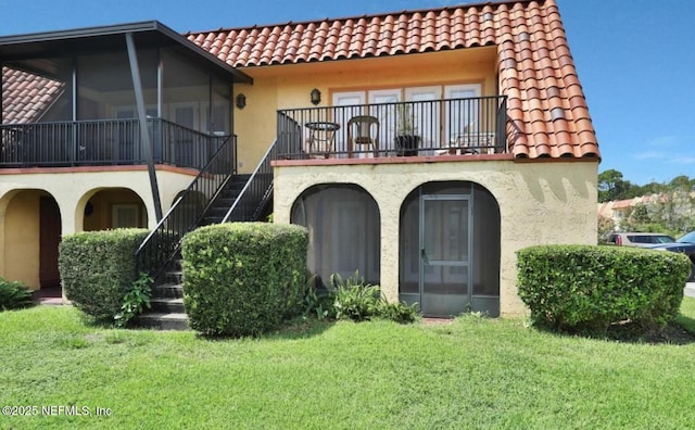 back of house with a balcony, a sunroom, and a lawn