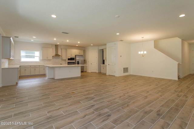 kitchen featuring stainless steel fridge with ice dispenser, open floor plan, wall chimney exhaust hood, recessed lighting, and decorative backsplash