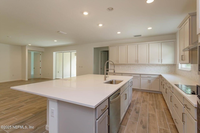 kitchen with a sink, stainless steel dishwasher, black electric cooktop, light wood-style floors, and a kitchen island with sink