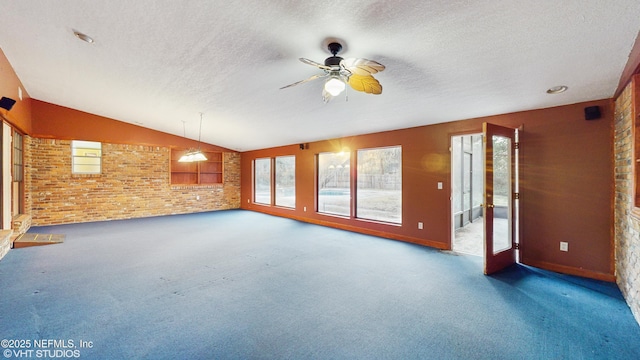 interior space featuring vaulted ceiling, dark carpet, brick wall, and ceiling fan