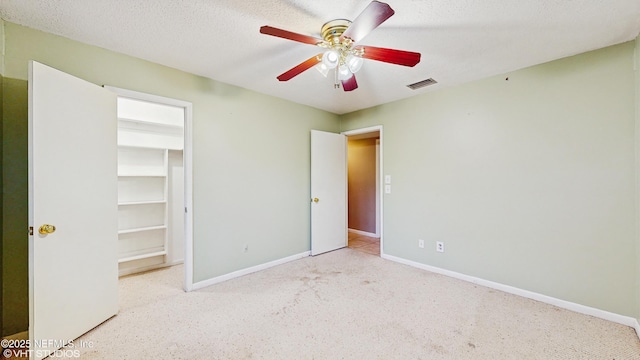 unfurnished bedroom featuring a walk in closet, ceiling fan, a textured ceiling, and a closet