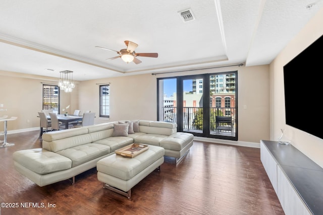 living room featuring dark hardwood / wood-style flooring, a tray ceiling, ceiling fan with notable chandelier, and a textured ceiling