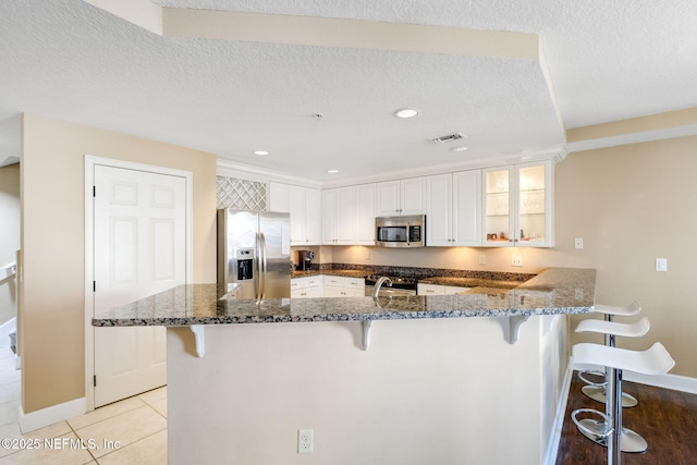 kitchen with white cabinetry, dark stone countertops, a kitchen bar, light tile patterned floors, and stainless steel appliances