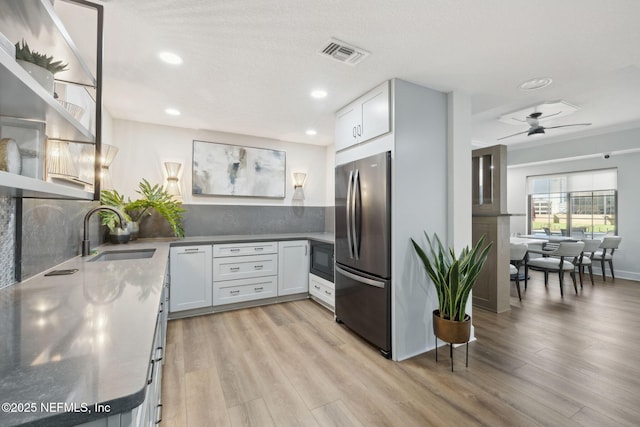 kitchen featuring tasteful backsplash, white cabinetry, black microwave, sink, and stainless steel fridge