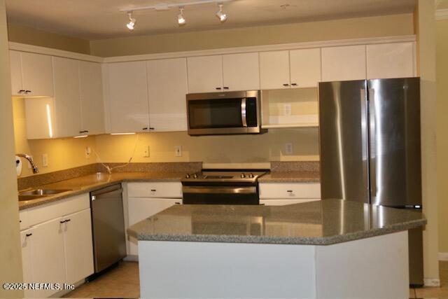 kitchen with stainless steel appliances, white cabinetry, a center island, and sink