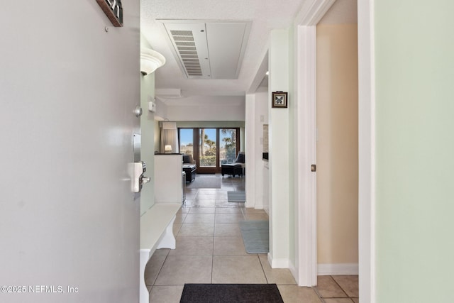 hall featuring light tile patterned floors, attic access, and baseboards