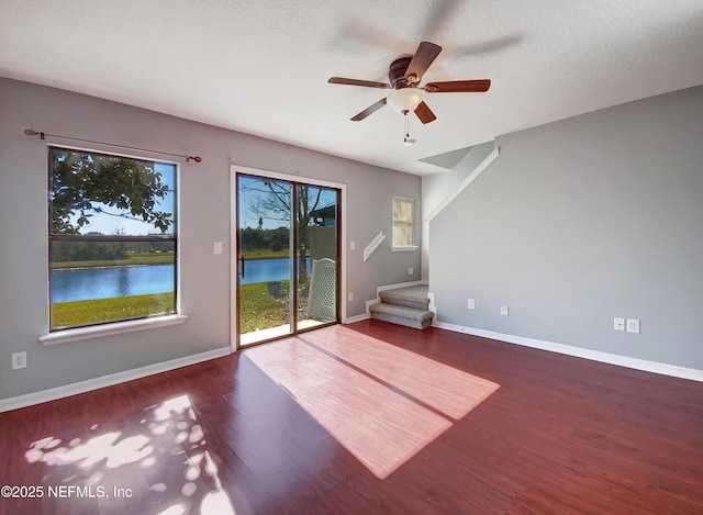 spare room with a textured ceiling, hardwood / wood-style flooring, a water view, and ceiling fan