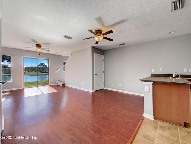 unfurnished living room featuring a textured ceiling, sink, hardwood / wood-style flooring, a water view, and ceiling fan