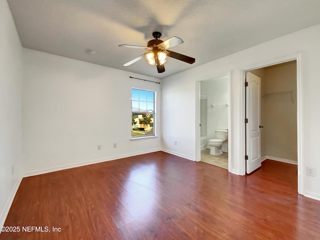 unfurnished bedroom featuring ensuite bathroom, ceiling fan, dark wood-type flooring, a walk in closet, and a closet