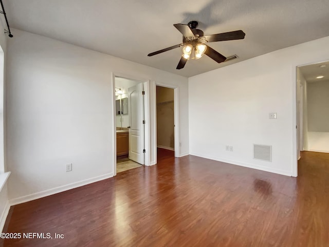 unfurnished bedroom featuring a walk in closet, ceiling fan, connected bathroom, and dark wood-type flooring