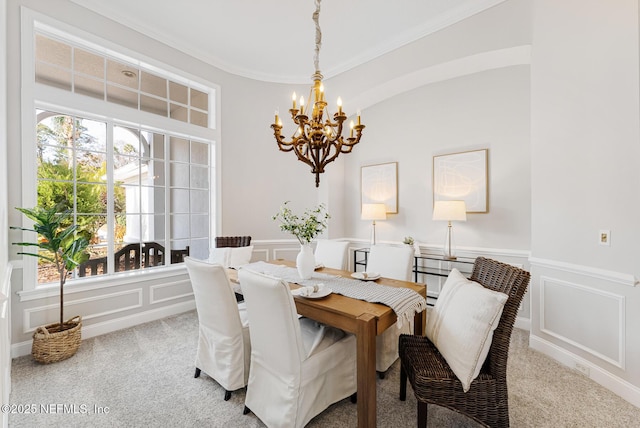 carpeted dining space with a chandelier, a wainscoted wall, a decorative wall, and ornamental molding