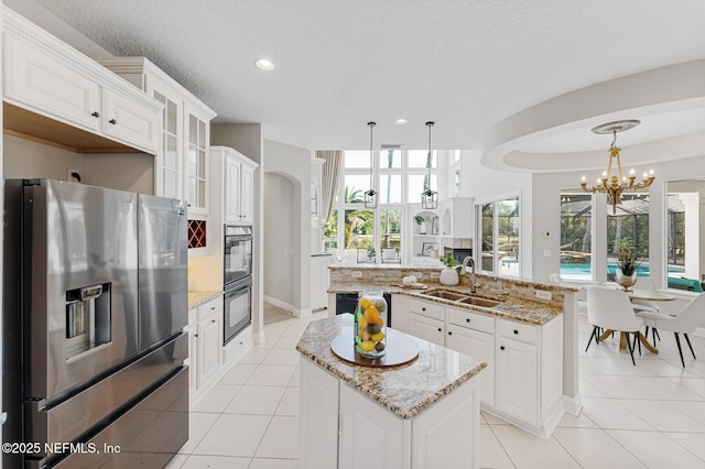 kitchen featuring glass insert cabinets, a kitchen island with sink, a sink, stainless steel fridge with ice dispenser, and decorative light fixtures