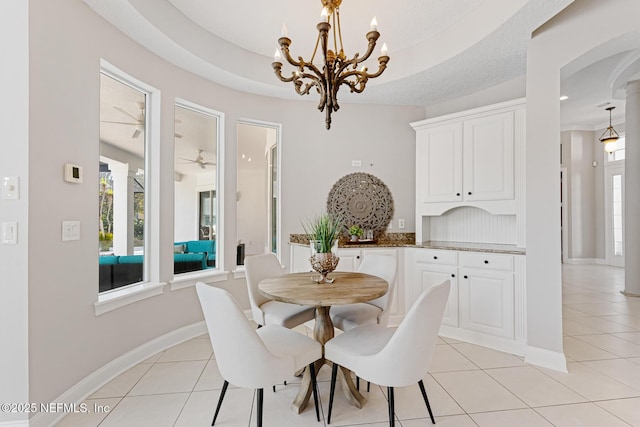 dining area with ceiling fan with notable chandelier, light tile patterned flooring, a raised ceiling, and baseboards