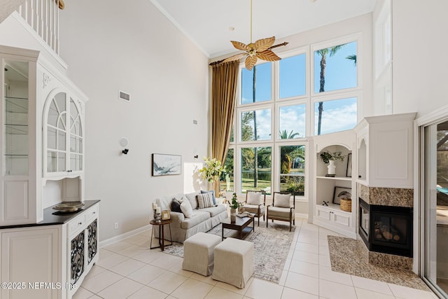 living area featuring crown molding, light tile patterned floors, a high ceiling, a multi sided fireplace, and baseboards