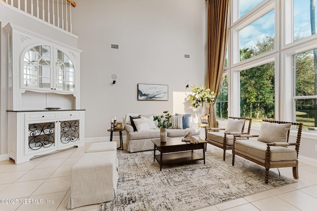 living area featuring baseboards, visible vents, a high ceiling, and light tile patterned floors