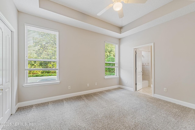 spare room featuring a ceiling fan, a tray ceiling, light colored carpet, and baseboards