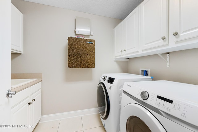 clothes washing area with light tile patterned floors, cabinet space, baseboards, washer and clothes dryer, and a textured ceiling