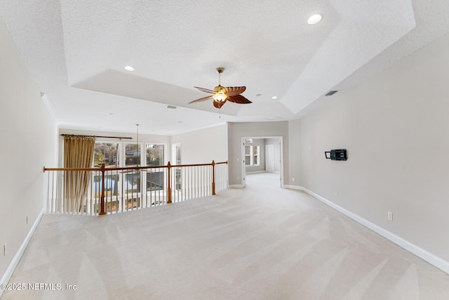 empty room with light carpet, a tray ceiling, a textured ceiling, and baseboards