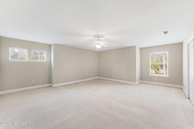 unfurnished room with light colored carpet, visible vents, ceiling fan, a textured ceiling, and baseboards