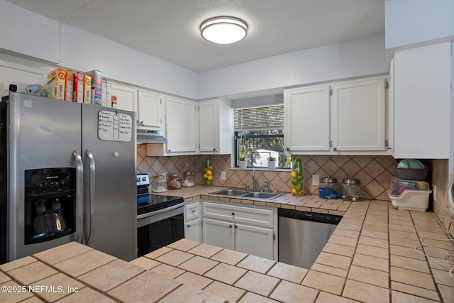 kitchen with white cabinetry, stainless steel appliances, tasteful backsplash, sink, and tile countertops