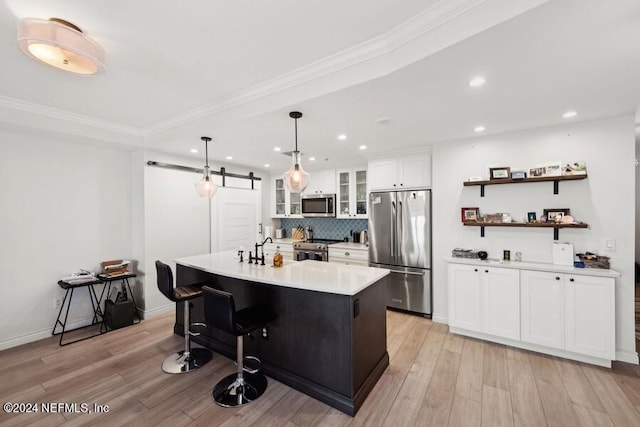 kitchen with hanging light fixtures, appliances with stainless steel finishes, white cabinetry, a barn door, and a center island with sink