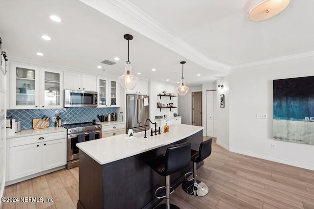 kitchen featuring an island with sink, white cabinetry, appliances with stainless steel finishes, and decorative light fixtures