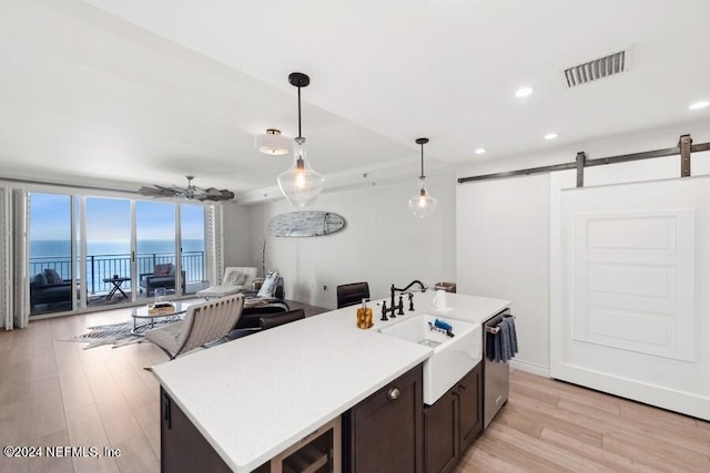 kitchen featuring decorative light fixtures, a water view, stainless steel dishwasher, a center island with sink, and a barn door