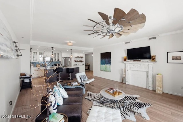 living room with a fireplace, light wood-type flooring, ceiling fan, and ornamental molding