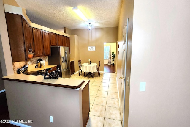 kitchen with appliances with stainless steel finishes, decorative backsplash, light tile patterned floors, kitchen peninsula, and a textured ceiling