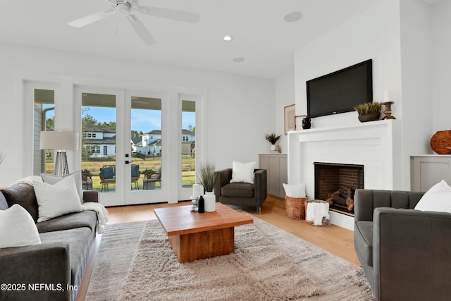 living room with ceiling fan, light hardwood / wood-style floors, a brick fireplace, and french doors