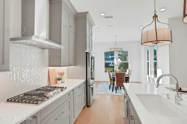 kitchen with appliances with stainless steel finishes, wall chimney exhaust hood, decorative light fixtures, light hardwood / wood-style floors, and sink