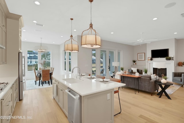 kitchen featuring appliances with stainless steel finishes, an island with sink, sink, hanging light fixtures, and light hardwood / wood-style flooring