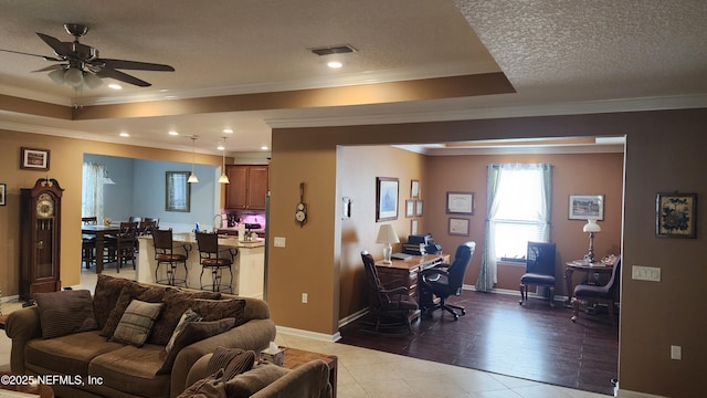 tiled living room featuring ceiling fan, ornamental molding, a raised ceiling, and a textured ceiling